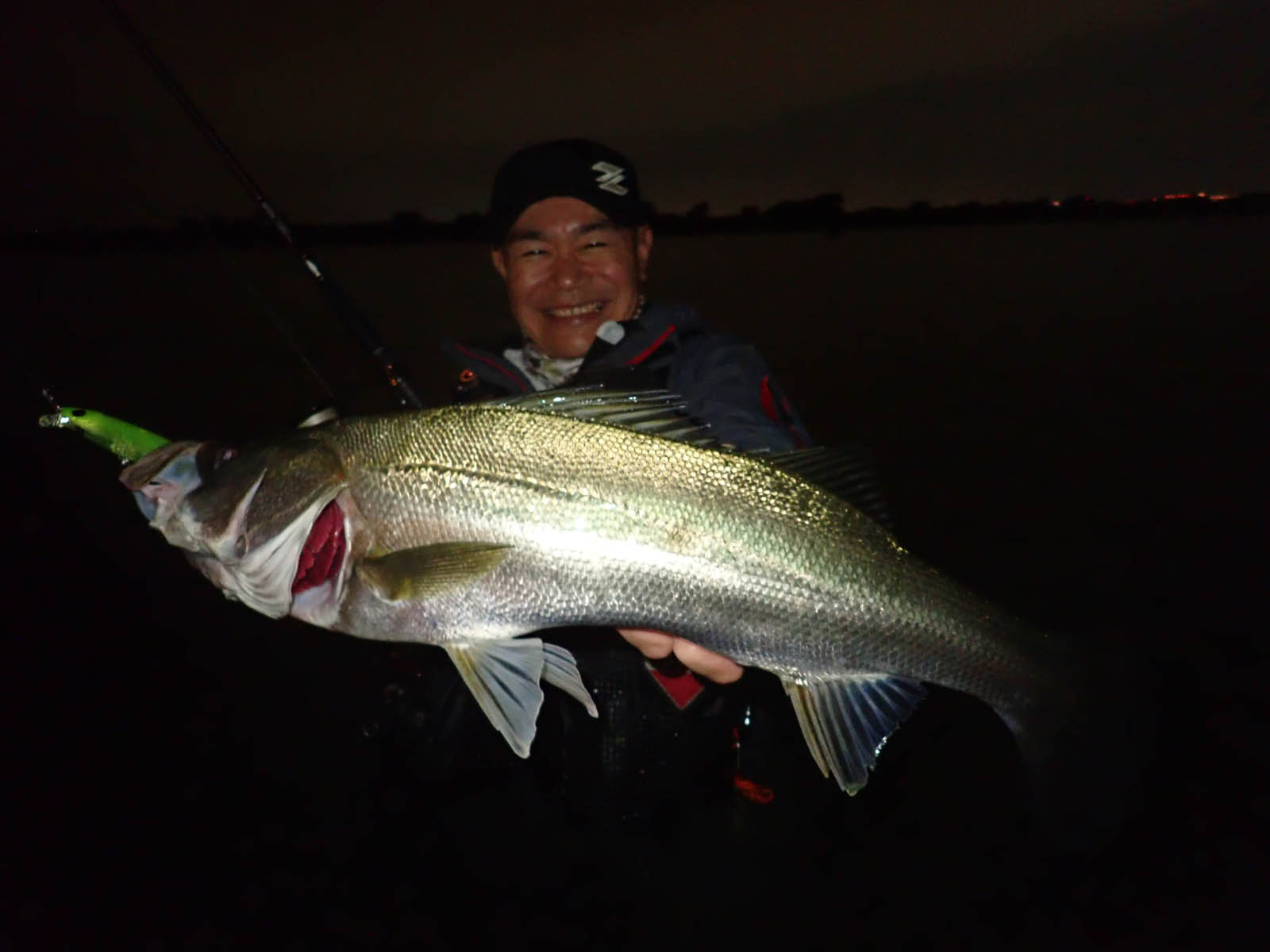 夜の河川で釣れたシーバスを持つ浅川和治さん