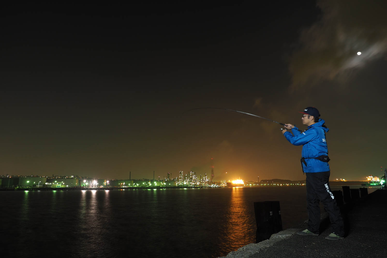 夜景の見えるベイエリアの岸壁で餌木を投げる釣り人