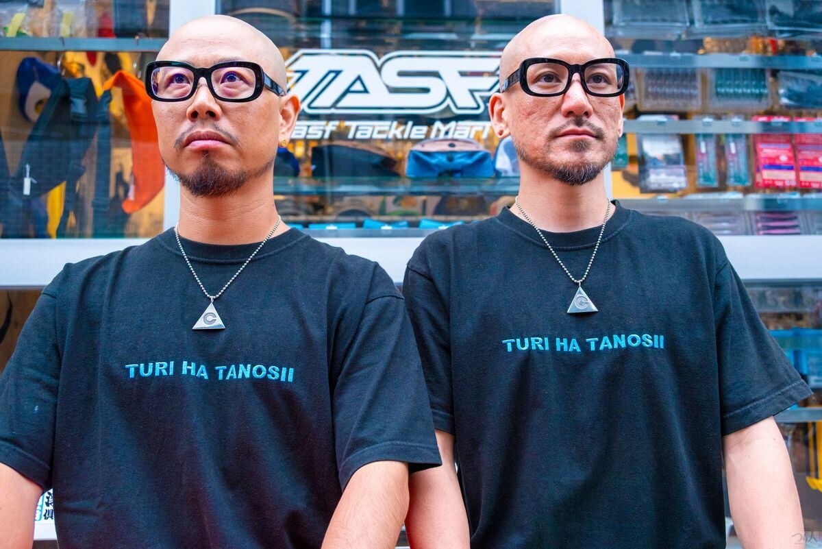 TASFのロゴの前に並ぶ山本健太さん（右）と安藤仁彦さん（左）