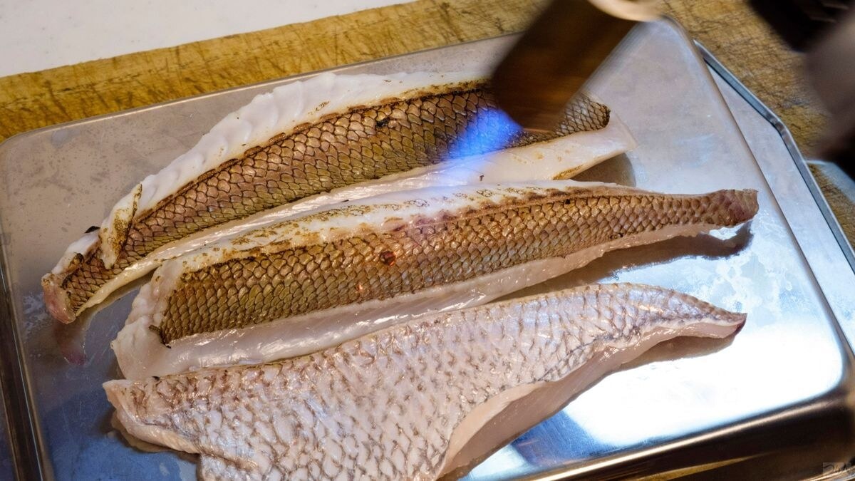 刺し身用の皮付き節身は調理用バーナーで皮目を焼き、焙りの身に仕上げてサイコロ状に切っておく